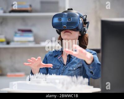 Donna che indossa occhiali e cuffie VR in un ufficio moderno Foto Stock