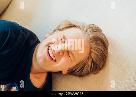 Vista dall'alto del ragazzo giocoso che giace sul divano Foto Stock