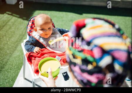 Madre che alimenta il bambino ragazzo seduto in sedia alta Foto Stock