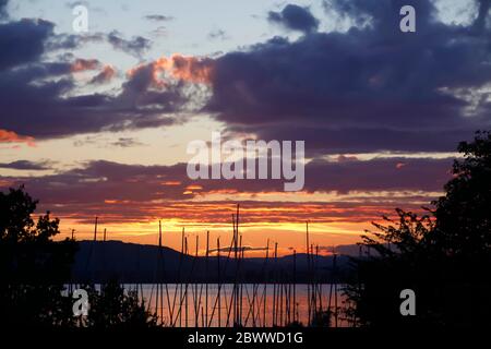Germania, Lago di Costanza, alberi di barche ormeggiate sul lungolago al tramonto nuvoloso Foto Stock