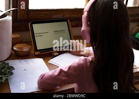 Ragazza che indossa cuffie che traducono le lingue su un tablet digitale mentre impara i fumetti a casa Foto Stock