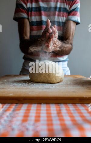 Mani dell'uomo che stendono la farina sulla palla da impasto Foto Stock