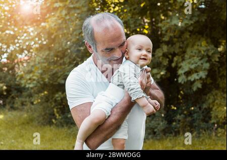 Uomo anziano sorridente che tiene la bambina sul braccio in un parco Foto Stock