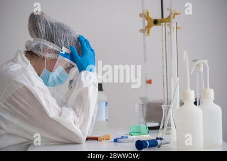 Scienziato stanco in abbigliamento protettivo seduto alla scrivania Foto Stock