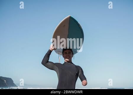 Surfista portatore di handicap che porta la sua tavola da surf in testa Foto Stock