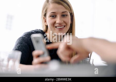 Ritratto di giovane donna sorridente e dito che punta sullo smartphone Foto Stock