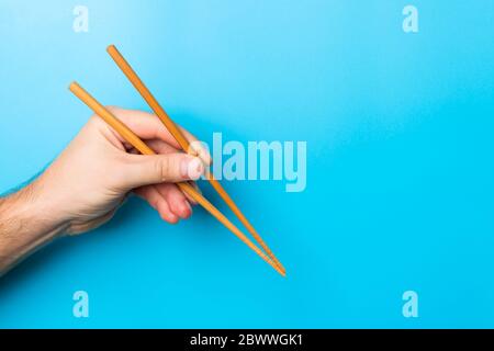 Immagine creativa delle bacchette di legno nelle mani di sesso maschile su sfondo blu. Il giapponese e il cinese del cibo con copia spazio. Foto Stock