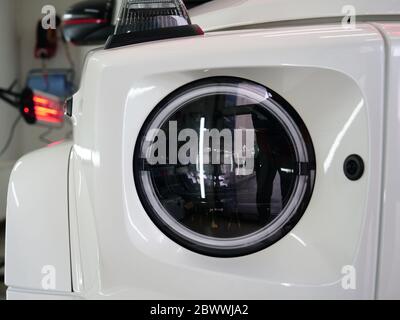 Di essiccazione a raggi infrarossi di parti di carrozzeria dopo applicazione di stucco e di vernice su un bianco off-road veicolo in officina di carrozzeria con lanterne rosse nella lavorazione Foto Stock