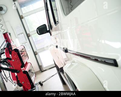 Di essiccazione a raggi infrarossi di parti di carrozzeria dopo applicazione di stucco e di vernice su un bianco off-road veicolo in officina di carrozzeria con lanterne rosse nella lavorazione Foto Stock