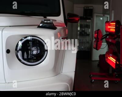 Di essiccazione a raggi infrarossi di parti di carrozzeria dopo applicazione di stucco e di vernice su un bianco off-road veicolo in officina di carrozzeria con lanterne rosse nella lavorazione Foto Stock