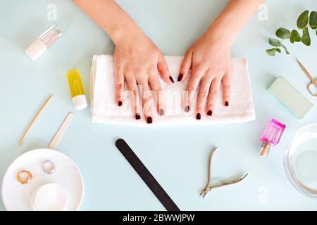 Vista dall'alto della femmina anonima con manicure scura seduta al tavolo con vari strumenti durante la procedura professionale di manicure nel salone termale Foto Stock