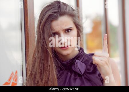 Attenzione, ascolti. Primo piano ritratto di giovane donna che tenti il dito isolato fuori città salone negozio muro sfondo. Emozione umana negativa Foto Stock