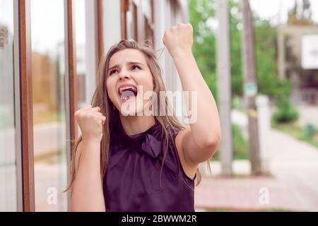 Ragazza fortunata. Closeup ritratto felice giovane donna felice esulti pompanti pugni estatico isolato all'aperto città sfondo negozio. Festeggia il concetto di successo. Foto Stock