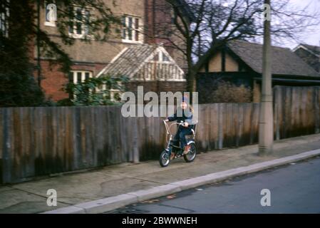 Una ragazza di 7 anni che indossa jeans blu, un cappello di lana blu con una bobina rossa e una giacca blu, che cavalca la sua bici Raleigh Tomahawk lungo il marciapiede nei sobborghi di Londra, Hatch End, Middlesex, UK Foto Stock