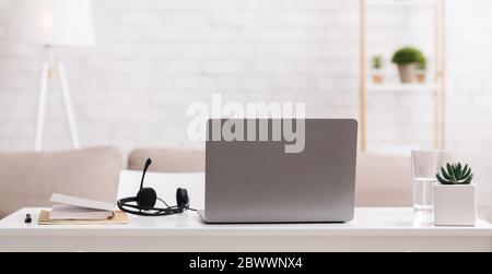 Consulenza online e lavoro remoto da casa. Sul tavolo sono presenti notebook, blocco note e cuffie con microfono Foto Stock