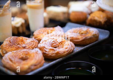 Primo piano di pasticceria fresca con glassa di latte sul tavolo del caffè del mattino. Anelli cotti con polvere di zucchero su sfondo nero sfocato Foto Stock