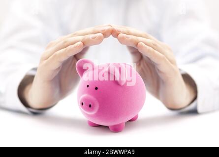 Proteggi i tuoi soldi. Piccolo banco di piggy rosa coperto da mani Foto Stock