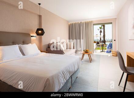 Interni dal design moderno della camera da letto dell'hotel con delicati arredi in tessuto e terrazza aperta con piscina tropicale Foto Stock