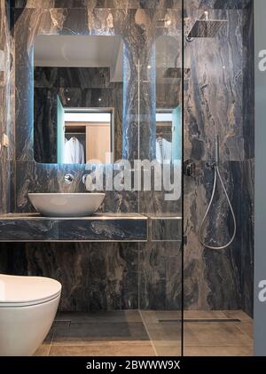 Vista frontale del moderno bagno in marmo grigio con lavandino con vasca, specchio, cabina doccia in vetro, parete in pietra e pavimento Foto Stock