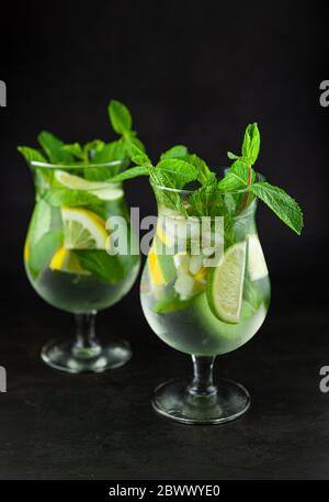 Mojito estivo con menta e calce rinfrescante cocktail con rum e ghiaccio in vetro su sfondo nero. Cocktail mojito su tavolo di pietra scuro. Vetro vetroso alto per Foto Stock