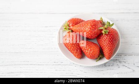 Poche fragole mature su piatto bianco su tavola di legno ciotola di fragola isolata su sfondo bianco piacere estivo Foto Stock