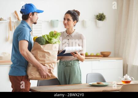 Uomo di consegna in uniforme che consegna il cibo alla donna mentre firma per la consegna Foto Stock