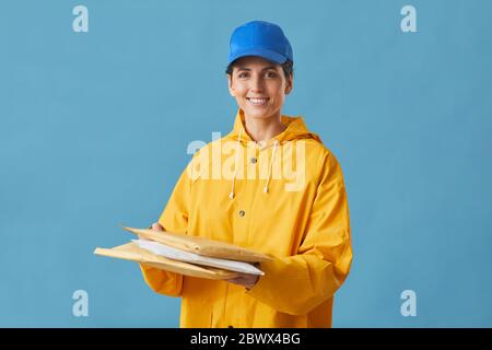 Ritratto di giovane donna in uniforme tenendo parcelle in mano e sorridendo a macchina fotografica isolata su sfondo blu Foto Stock