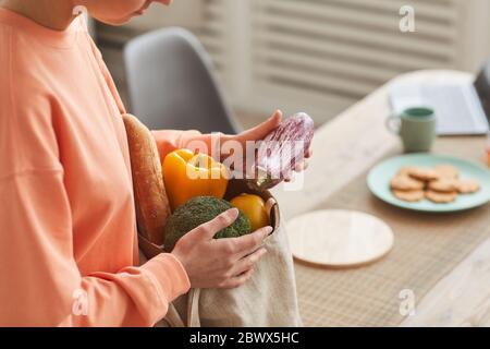 Primo piano di giovane donna che taccherà le verdure fresche dalla borsa di carta in cucina Foto Stock