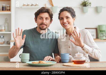 Ritratto di giovane coppia felice che ha fatto colazione e sorridendo alla macchina fotografica mentre si siede al tavolo in cucina Foto Stock