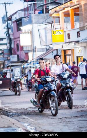 Le motociclette a volte con intere famiglie si fanno strada attraverso le strade polverose di Coron Town proprio sull'isola di Coron, Palawan, le Filippine. Foto Stock