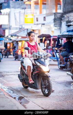 Le motociclette a volte con intere famiglie si fanno strada attraverso le strade polverose di Coron Town proprio sull'isola di Coron, Palawan, le Filippine. Foto Stock