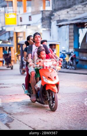 Le motociclette a volte con intere famiglie si fanno strada attraverso le strade polverose di Coron Town proprio sull'isola di Coron, Palawan, le Filippine. Foto Stock