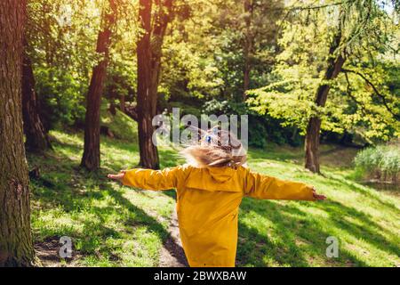 Donna felice in impermeabile giallo che corre saltando sentendosi camminare libero nel parco estivo. Ragazza che si diverte all'aperto Foto Stock