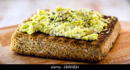 Avocado su toast croccante, con condimenti e spezie. Pane vegano fatto da lievito biologico. Foto Stock