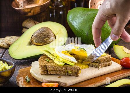 toast all'avocado tagliato a mano con uova fritte a metà, gocce di tuorlo. Colazione sana. Foto Stock