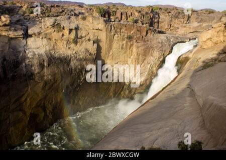 La cascata di Augrabies nel pomeriggio, con un arcobaleno alla base dove si tuffano nella gola del fiume Orange Foto Stock