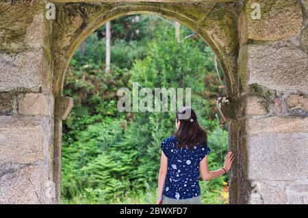 Ragazza sotto una porta di pietra che esce in una foresta. Questo è situato in un punto panoramico alto a Poio, Pontevedra, Galizia, Spagna. Foto Stock