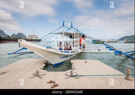 Una barca di pescatori dalla coda lunga carica di rifornimenti e turisti per fare una gita di un giorno con una enorme petroliera alle spalle dell'isola di El Nido, Filippine. Foto Stock