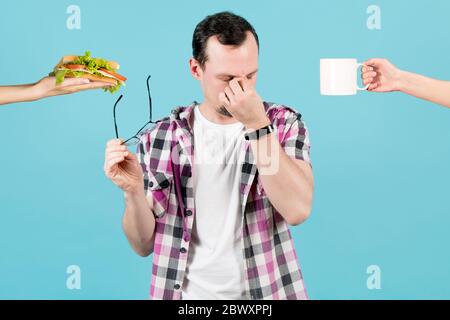 l'uomo stanco viene offerto uno spuntino. Le mani della donna tengono fuori per l'uomo un panino e una tazza di tè, l'uomo tolse i suoi occhiali e sfregò gli angoli degli occhi Foto Stock