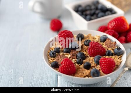 Granola con mirtilli e lamponi in ciotola bianca su scrivania di colore bianco scuro. Foto Stock