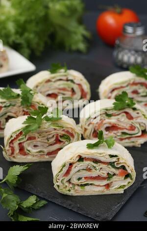 Pita roll con pollo affumicato, pomodori e formaggio situato su sfondo scuro su un piatto di ardesia, orientamento verticale, primo piano Foto Stock