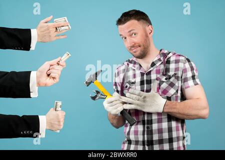 un lavoratore duro con gli attrezzi nelle sue mani tira un guanto protettivo dalla sua mano e sorride perché le mani di bei uomini gli tengono fuori i soldi. highl Foto Stock
