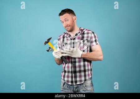 Un lavoratore sporco e duro in una camicia intelligente con gli attrezzi in mano tira un guanto protettivo dalla sua mano e sorride con precisione Foto Stock