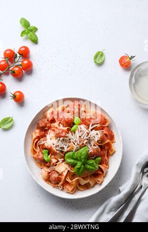 Fettuccine di pasta italiana fatta in casa con polpette, formaggio, pomodori, basilico su tavola bianca. Vista dall'alto. Formato verticale. Foto Stock