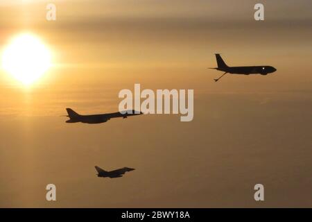 Un aereo bombardiere furtivo della US Air Force B-1B Lancer della 28a Bomb Wing, sono scortati dai combattenti britannici RAF Typhoon FGR4s, silhoueted dal sole che tramonta il 20 maggio 2020 sul Regno Unito. Foto Stock