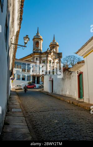 Scena di strada con la chiesa di San Francesco d'Assisi l'ex città mineraria coloniale Ouro Preto, ex Vila Rica, una città nello stato di Minas Gerais Foto Stock