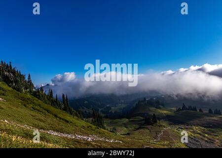 spesse nuvole bianche soffici che gettano ombre su un paesaggio di montagna verde sotto un cielo blu luminoso Foto Stock