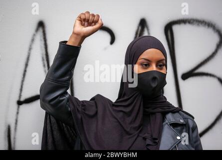 La donna, indossando un hijab e una maschera facciale, solleva il pugno di fronte a un muro di graffiti etichettato durante la marcia di protesta del Regno Unito Black Lives Matter. Londra, Regno Unito Foto Stock