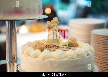 Torta di nozze bianca in piedi sul tavolo festivo. Primo piano di figurine di top di sposa e di sposo. Concetto di giorno di nozze. Foto Stock