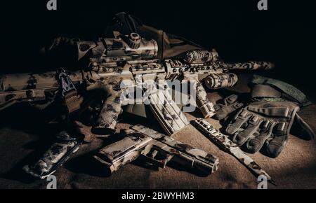 Foto di fucile militare mimetato che si stesa su un telo da tavolo con pistola, coltello e guanti tattici. Foto Stock